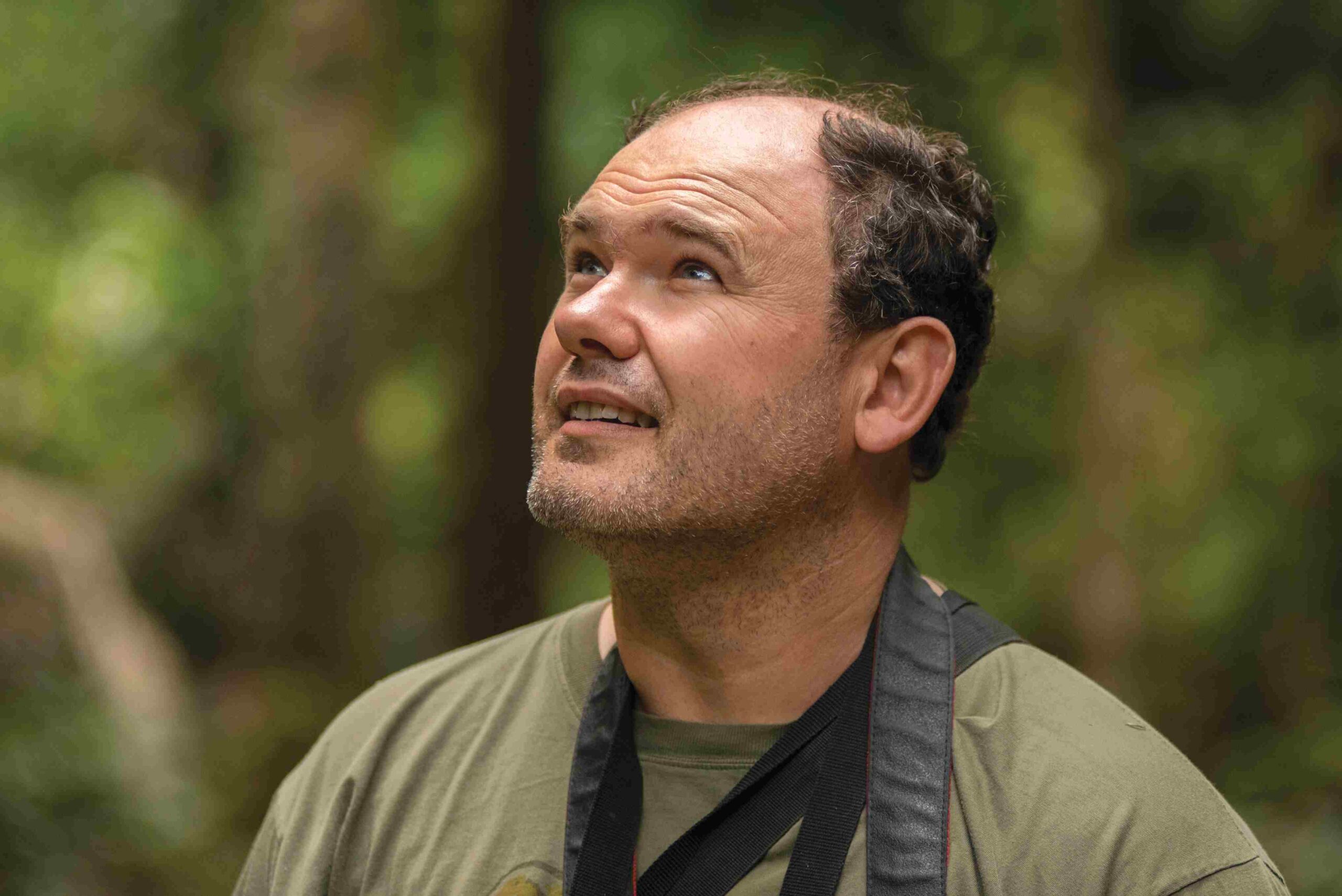 A photo of a middle-aged, masculine person with light skin and short, grey hair standing outside.