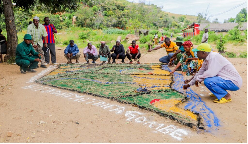 A photo of about ten people standing outside around a map on the ground made of colorful stones.