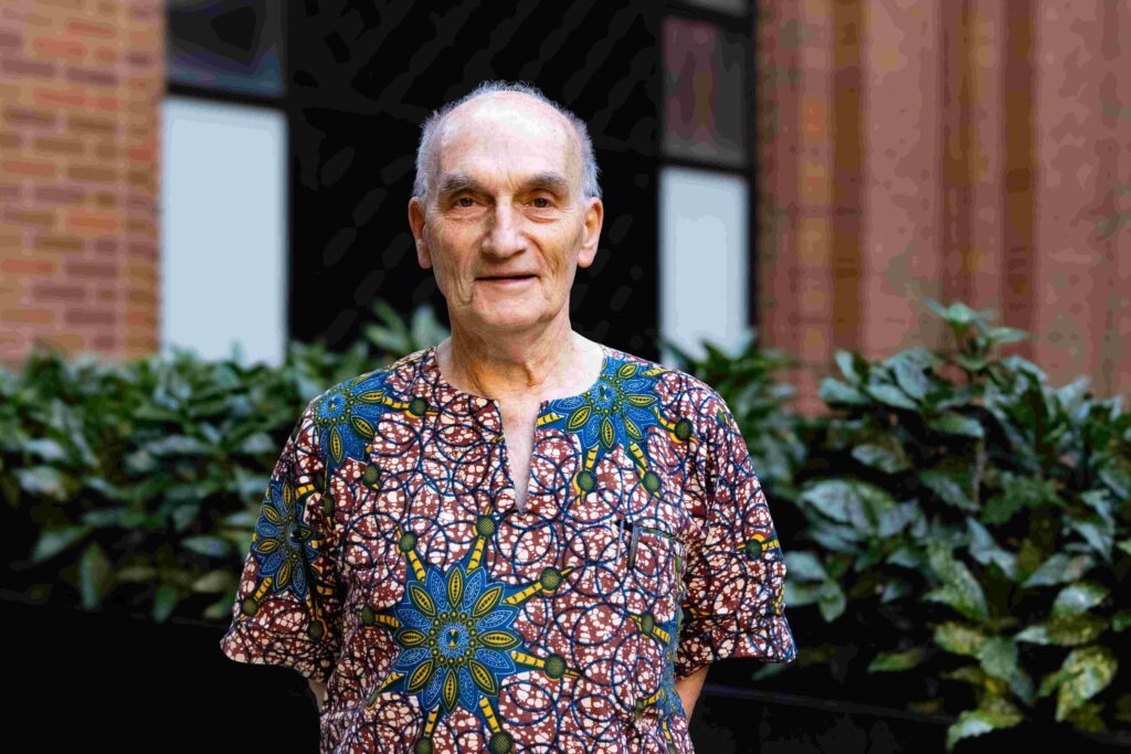 Dr Anthony Collins, smiling, wearing a multicolored, multi-patterned shirt in an urban setting.