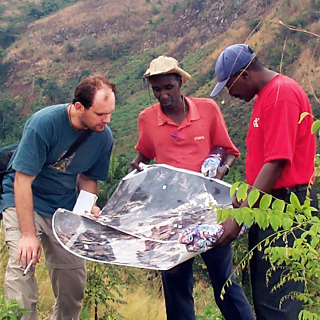 Three men stand around a map on a hillside of Gombe National Park.