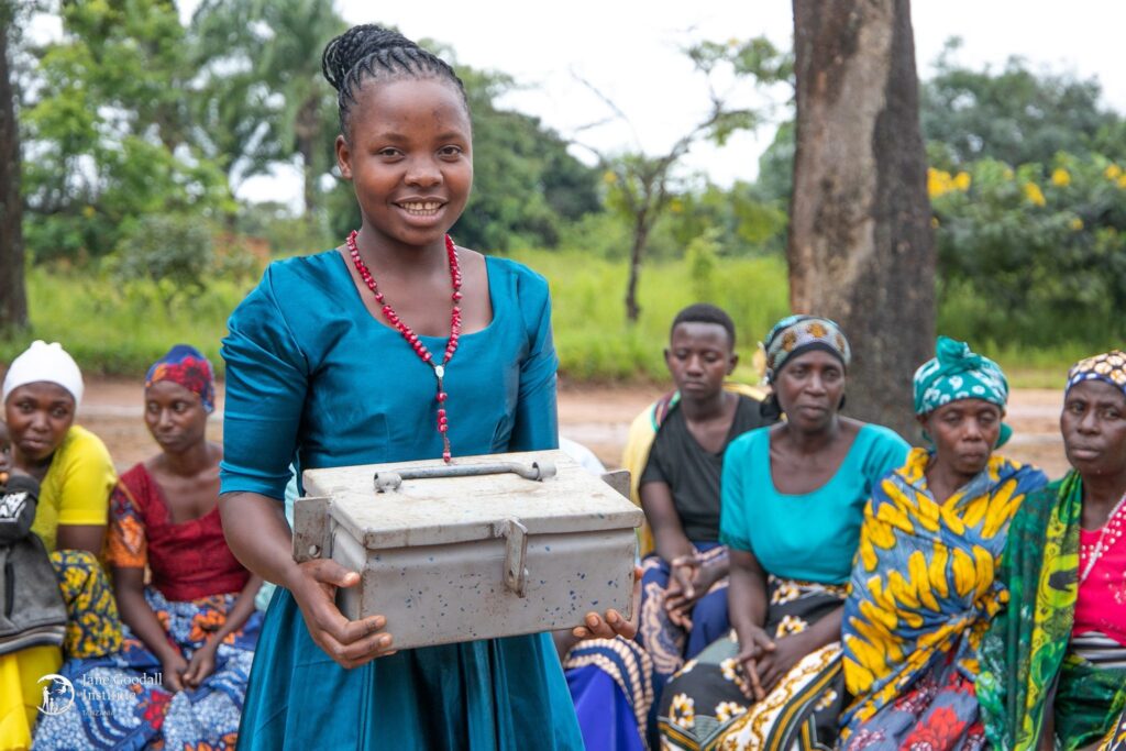 A photo of a young, feminine person with dark skin and black hair in a bun holding up a metal lockbox.