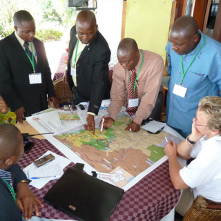 A group of men in collared shirts stand around a table, focused on a large map.