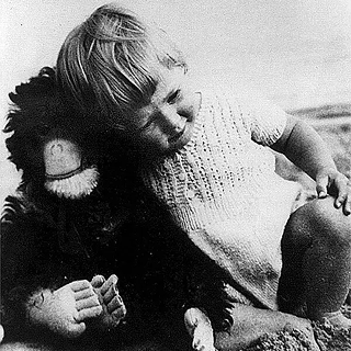 An infant Jane Goodall hugging a chimpanzee plush doll.