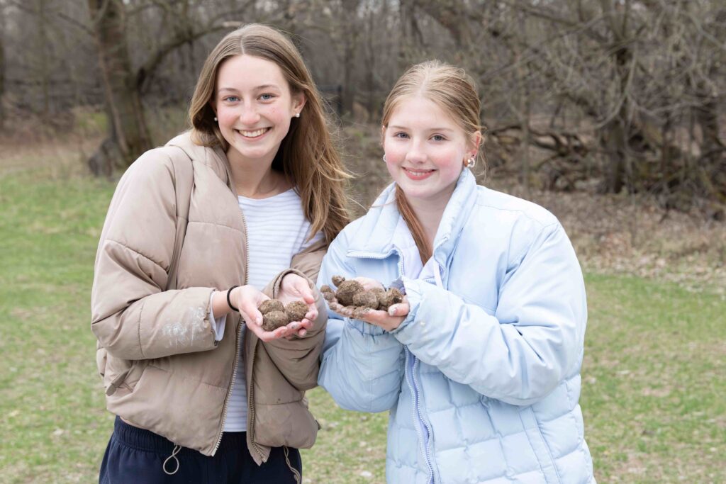 Two young girls of light complexion hold seed balls on a cold fall day.