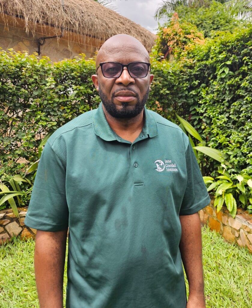 Emola Pippen-Hashim wearing a green JGI collared shirt in front of green bushes in an outdoor space.