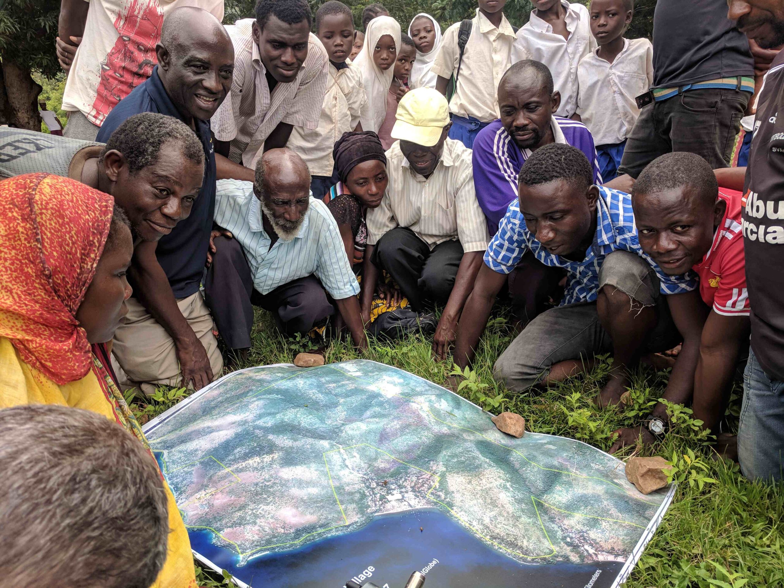 A photo of about twenty people with dark skin and black hair gathered around a map on the floor.